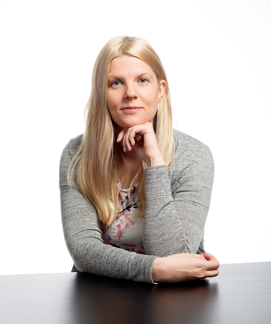 Sosiaalityön asiantuntija Riikka Mettälä nojaa leukansa toiseen käsivarteen ja hymyilee kameralle.
