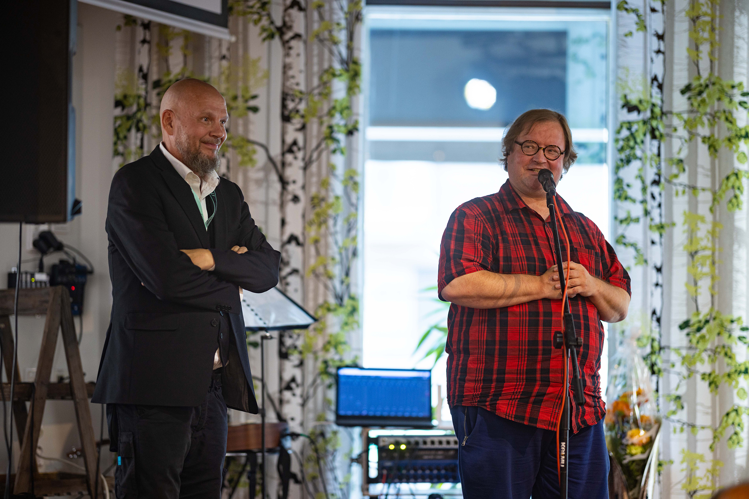 Olavi Sydänmaanlakka ja Janne Jalava seisovat lavalla ja hymyilevät yleisölle. Janne pitää puhetta mikrofonin edessä.