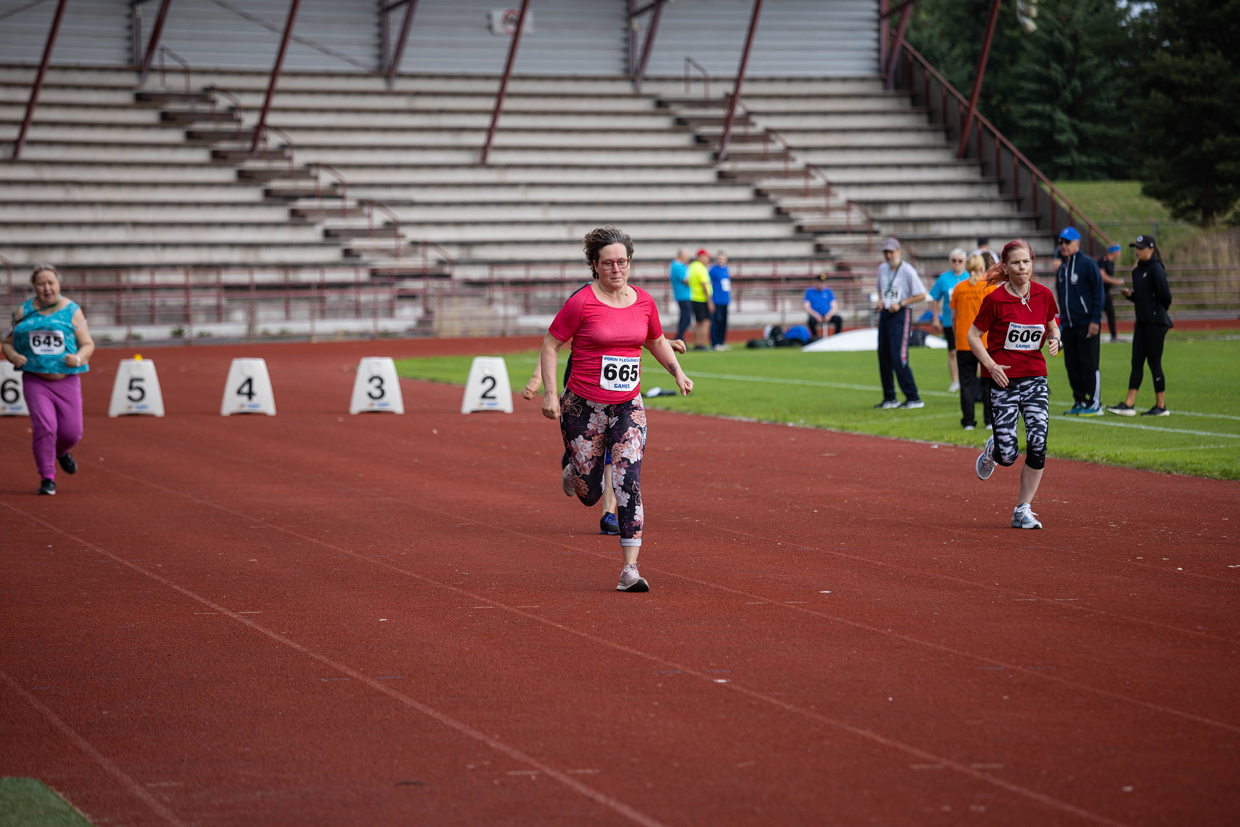 Kolme naista juoksee yleisurheilukentän juoksuradoilla kohti maalia.