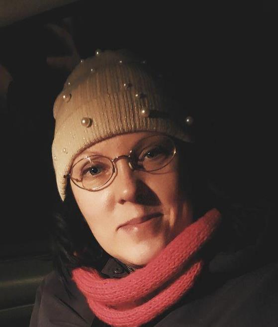 Anniina Holma-Suutari hymyilee pimeässä illassa. Hänellä on päässään helmikoristeinen pipo ja kaulassaan punainen huivi.