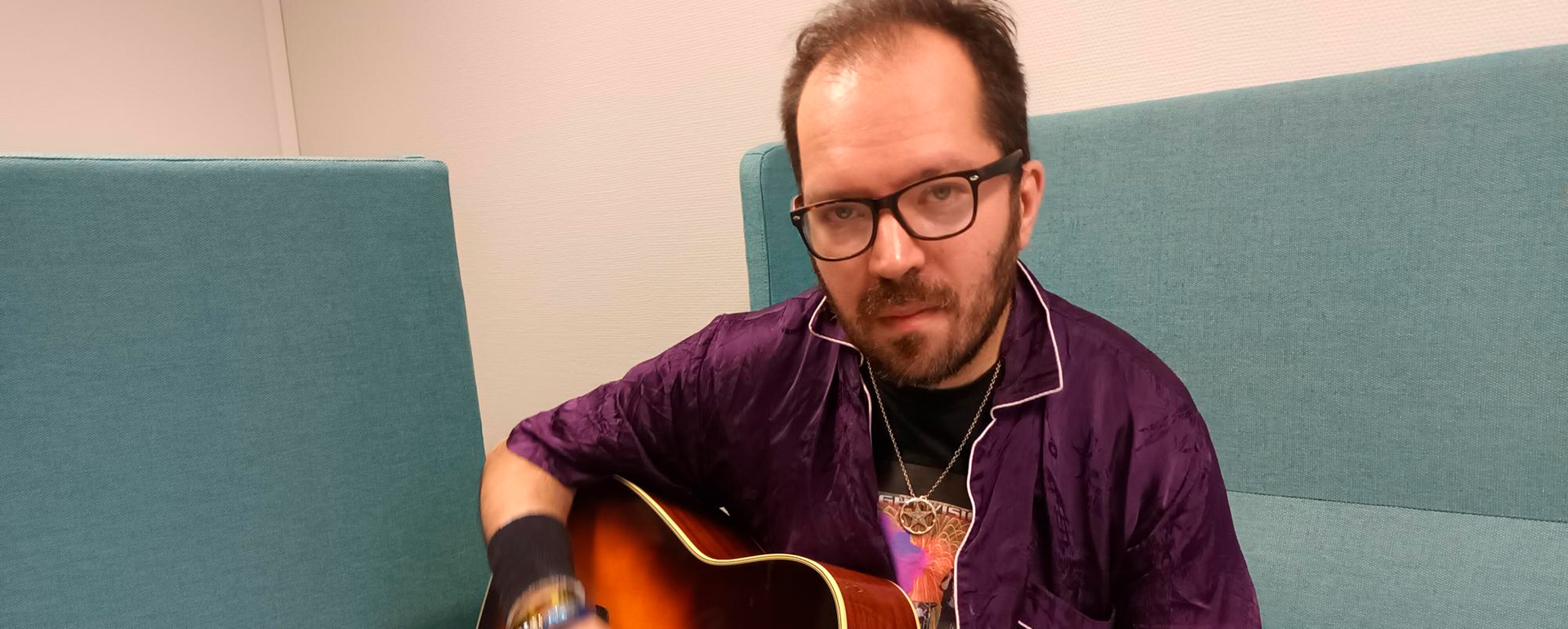 Riku Turpeinen soittaa kitaraa sohvalla.