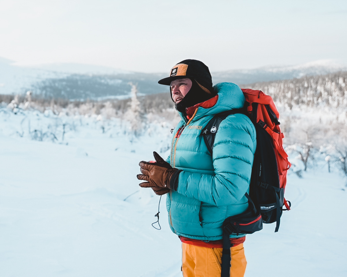 Teemu Suominen on lumisessa luonnossa. Selässään hänellä on rinkka ja yllään lämpimät ulkoiluvarusteet sekä kauluri vedetty leuan suojaksi.